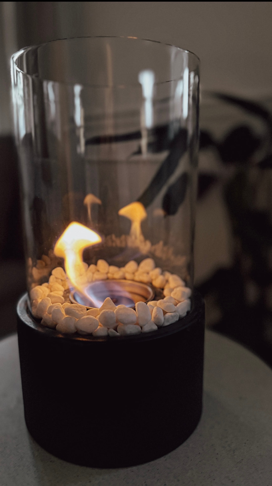 Small glass tabletop fireplace with white stones and a lit flame